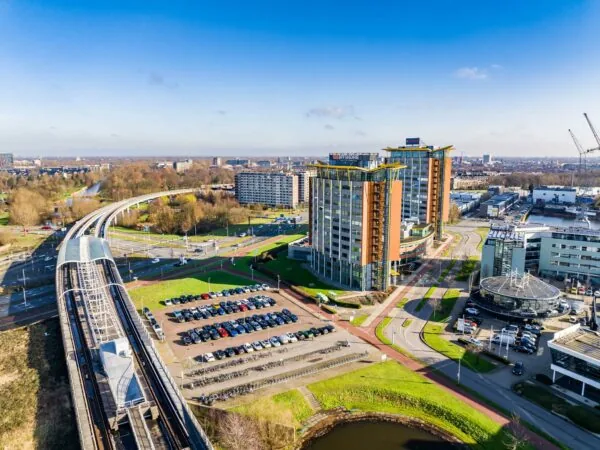 Luchtfoto van de Karel Doormanweg in een modern zakendistrict met hoge kantoorgebouwen, een metrostation, parkeerplaatsen en fietspaden.